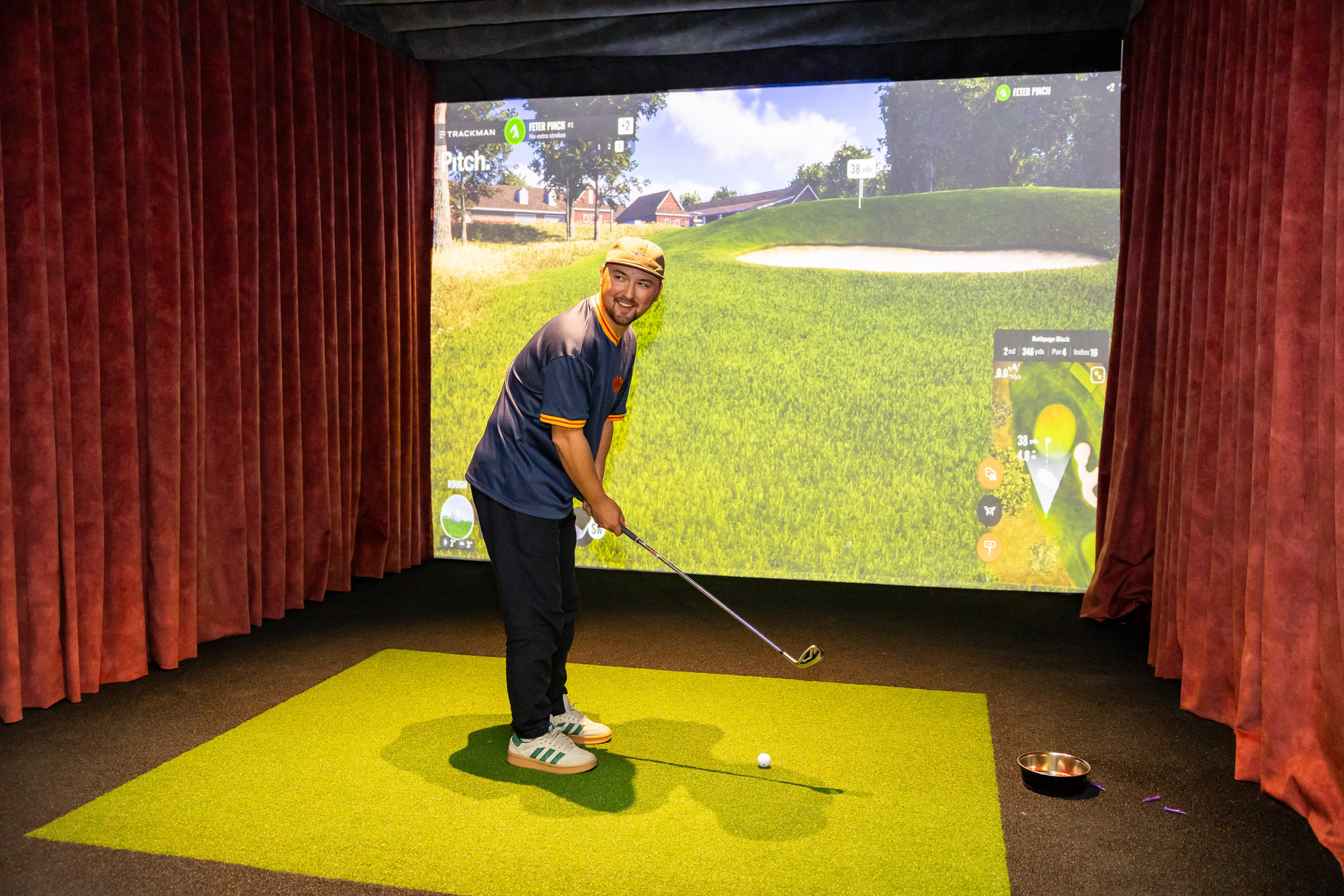Man in one of the golf bays with a golf club, in front of the trackman screen